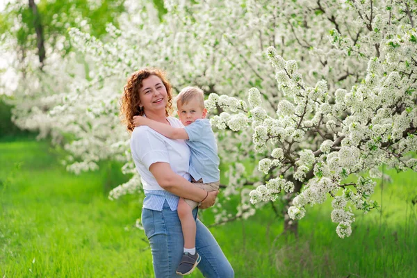 Мать держит своего маленького сына в цветущем весеннем саду. родительская любовь и забота — стоковое фото