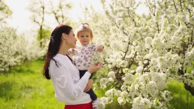 Parkta, çiçek açan ağaçların yanında kollarında küçük bir kızı olan anne.. 