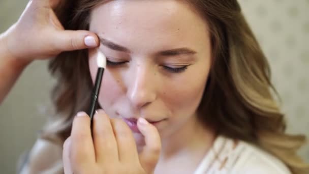Een mooi meisje met lang haar doen oog make-up. — Stockvideo