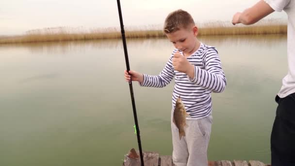 Мальчик поймал маленькую рыбку на удочке. рыбалка с детьми. — стоковое видео