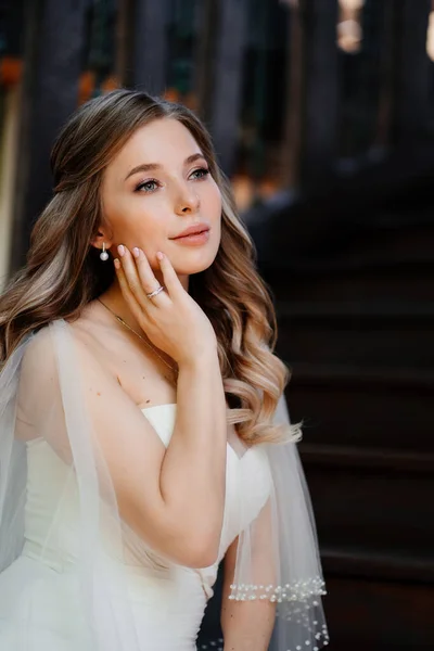 Hermosa y gentil novia se sienta en una escalera de madera oscura. —  Fotos de Stock