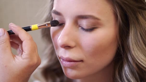 En vacker flicka med långt hår gör ögonmakeup. — Stockvideo