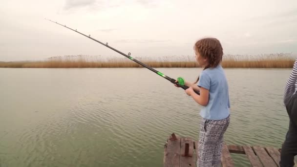 A little girl stands with a fishing rod on a bridge by the river. — Stock Video