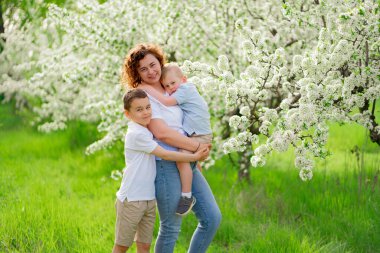 Çiçek açan bahçede oğulları olan bir anne. Kollarındaki en küçük çocuk