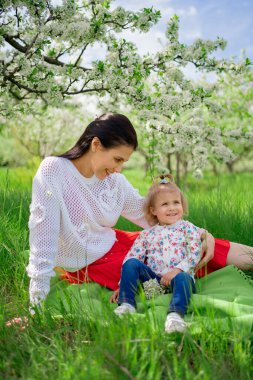 Anne ve kızı parkta çimenlikte çiçek açan bir ağacın yanında pikniğe gitmişler.. 