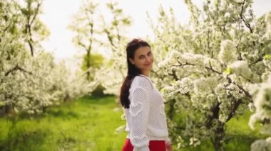 Güzel genç bir kadın çiçek açan ağaçların yanından geçiyor. Doğal kozmetik ürünleri ve parfümler. 