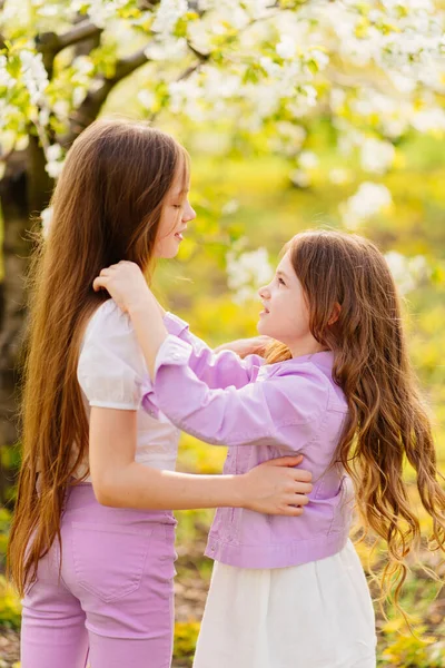 Dwie dziewczyny siostry bawić się i przytulać w ogrodzie z kwitnących drzew. — Zdjęcie stockowe