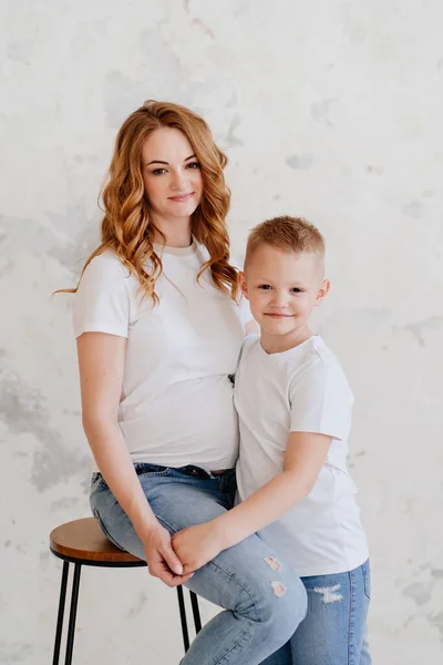 Gravid mor med son i vita t-shirts och jeans. Lycklig familj. — Stockfoto