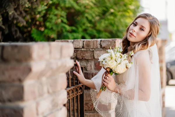 Schöne Braut mit einem Blumenstrauß am Zaun. — Stockfoto