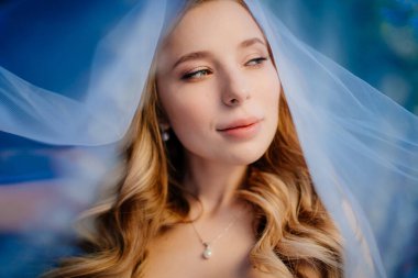 Duvağın altında uzun dalgalı saçları olan güzel bir gelin. Düğün makyajı.. 