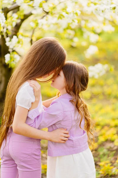 Zwei Mädchen Schwestern haben Spaß und kuscheln im Garten mit blühenden Bäumen. — Stockfoto