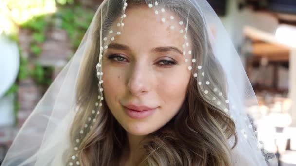 Hermosa novia con el pelo ondulado largo bajo el velo. Maquillaje de boda. — Vídeos de Stock