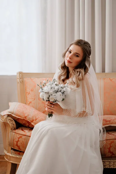 Porträt einer schönen Braut mit einem Strauß auf der Couch. Hochzeitstraditionen. — Stockfoto