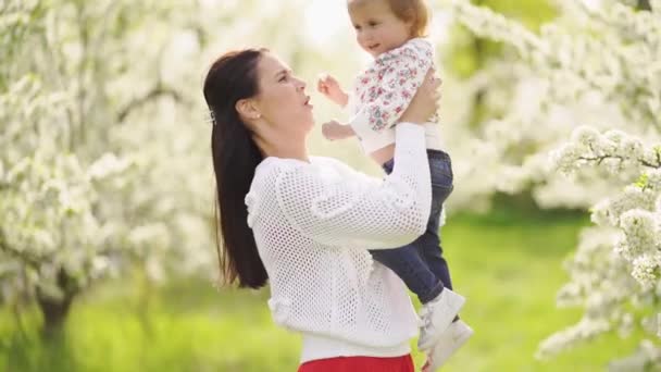 Mom throws up her daughter in the park by a flowering tree. happy childhood. — Stock Video