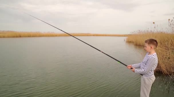 Chłopiec w pasiastych ubraniach łapie rybę na wędce.. — Wideo stockowe
