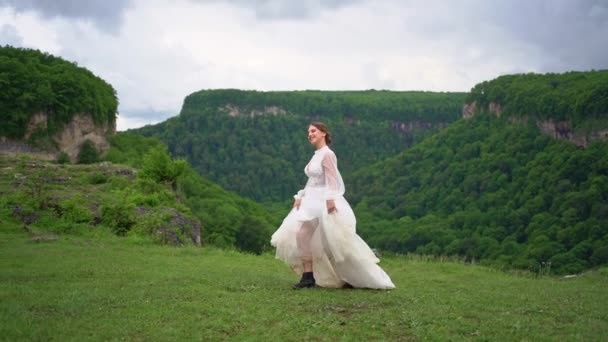 Una chica en un vestido de novia y botas negras va al césped en las montañas. — Vídeos de Stock