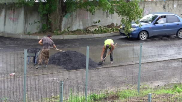 Trabajadores con una pala y una carretilla ponen asfalto en un camino mojado. — Vídeos de Stock