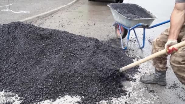 Pala de trabajador pone asfalto en una carretilla. camino mojado. — Vídeos de Stock