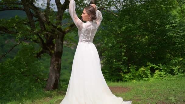 Hátsó kilátás gyönyörű fiatal nő egy esküvői ruha az erdőben a hegyekben — Stock videók