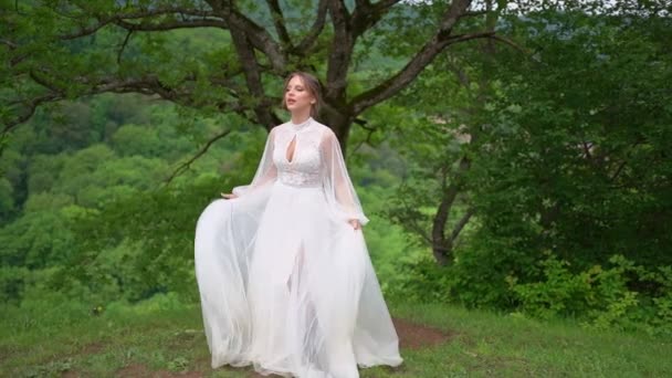 Boldog gyönyörű fiatal nő egy esküvői ruha az erdőben a hegyekben — Stock videók
