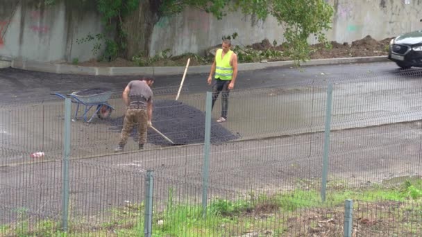 Werkers met een schop en een kruiwagen zetten asfalt op een natte weg. — Stockvideo