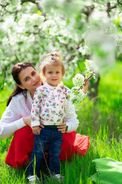 Anne ve küçük kızı parktaki çimenlikte çiçek açan bir ağacın yanında.. 