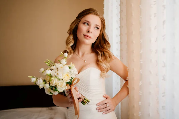 Retrato de uma bela noiva com um buquê à janela. Tradições de casamento. — Fotografia de Stock