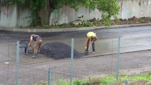 Рабочие с лопатой и тачкой положили асфальт на мокрую дорогу. — стоковое видео