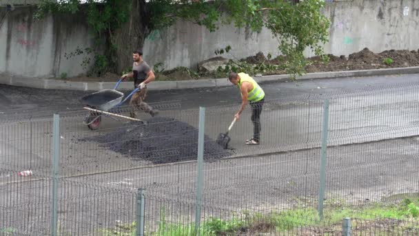 Trabajadores con una pala y una carretilla ponen asfalto en un camino mojado. — Vídeos de Stock