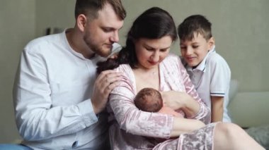 Yatak odasında yeni yürümeye başlayan çocukla mutlu bir aile. Annem emziriyor. 