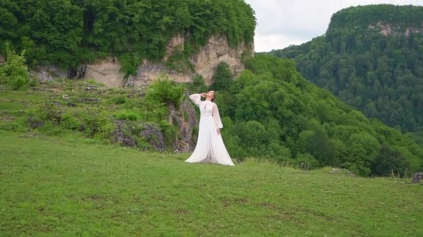 Una joven con un vestido de novia y botas negras posando en las montañas. — Vídeos de Stock