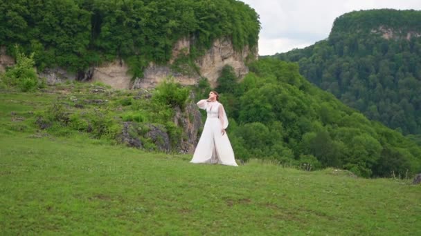 Uma mulher em um vestido de noiva e botas pretas posando nas montanhas. — Vídeo de Stock