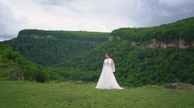 A woman in a wedding dress and black boots dances in the mountains. 