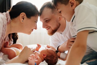 Evde yeni doğmuş bir bebeğin ilk günü. Mutlu aile yatak odasında yeni doğan bebeğe bakıyor.