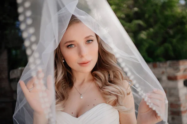 Glückliche Braut mit langen welligen Haaren unter dem Schleier draußen. Hochzeits-Make-up. — Stockfoto