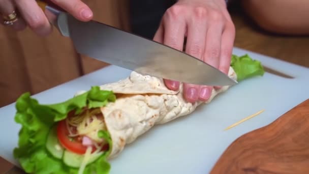 Kvinders hænder skåret i halv pita med grøntsager og ost på et skærebræt. – Stock-video