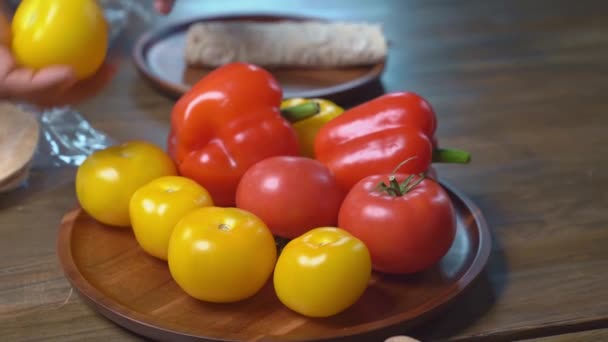 Руки красиво разбрасывают помидоры и сладкий перец на деревянной круглой доске — стоковое видео