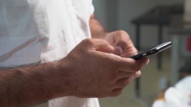 Beyaz tişörtlü bir adam akıllı bir telefon tutar ve bir mesaj yazar..