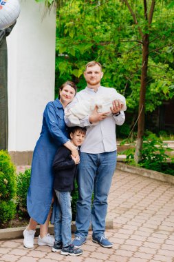 Anne ve baba yeni doğmuş bir bebek ve en büyük çocuk hastanenin çıkışında duruyorlar.