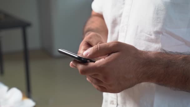 Un uomo con una camicia bianca tiene uno smartphone e scrive un messaggio. — Video Stock