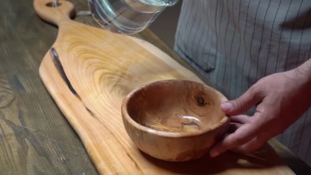 In una boccia di legno versano l'acqua da una caraffa di vetro. — Video Stock