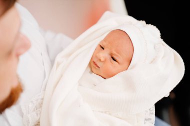 Beyaz elbiseli yeni doğmuş bir bebek, ailesinin elinde. Hastaneden taburcu olmak için.