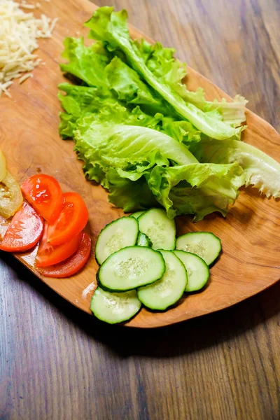 Салат, томаты с кольцами и огурцы на деревянной доске. — стоковое фото