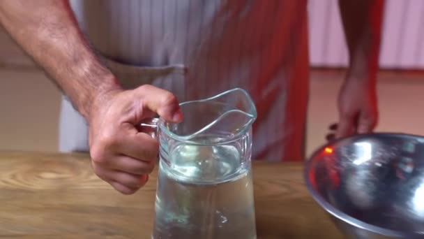 The man pours water from the glass carafe into a stainless steel bowl. — Stock Video