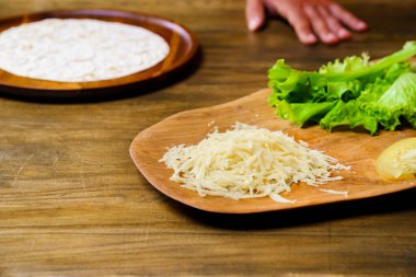 Tahta kesme tahtasında rendelenmiş peynir. Pide, marul ve doğranmış domates.