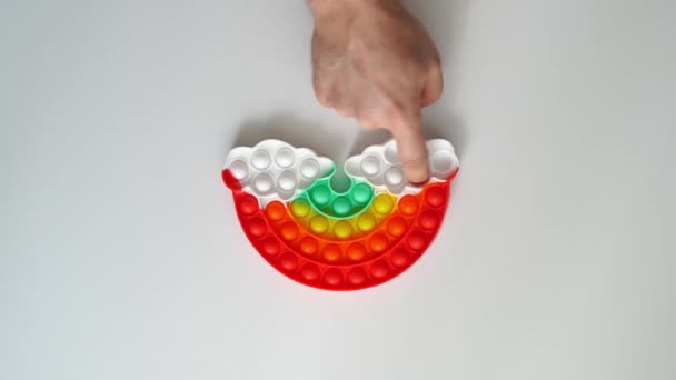 Mão joga com um brinquedo anti-stress multi-colorido na forma de um arco-íris. — Vídeo de Stock