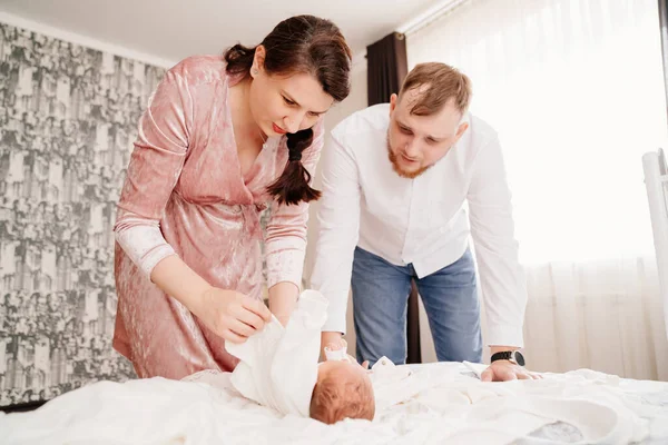 Padres jóvenes cambian a su bebé recién nacido en una cama en el dormitorio. — Foto de Stock