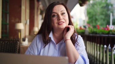 Mutlu kadın laptopuyla caddedeki kafede oturuyor, arkadaşıyla iletişim kuruyor.