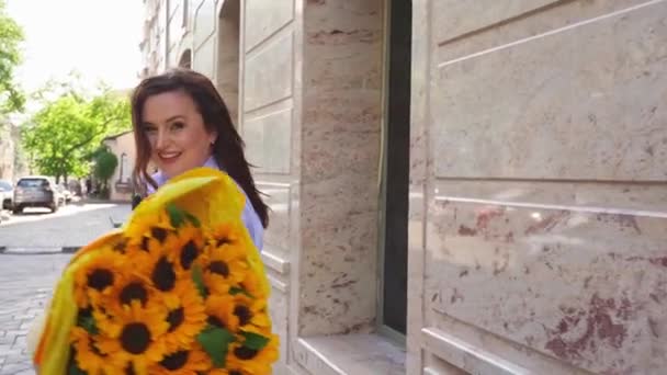 Mujer feliz con enorme ramo de girasoles decorativos paseos por la calle de la ciudad — Vídeos de Stock