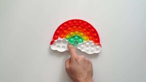 Hand plays with a multi-colored anti-stress toy in the shape of a rainbow. — Stock Video